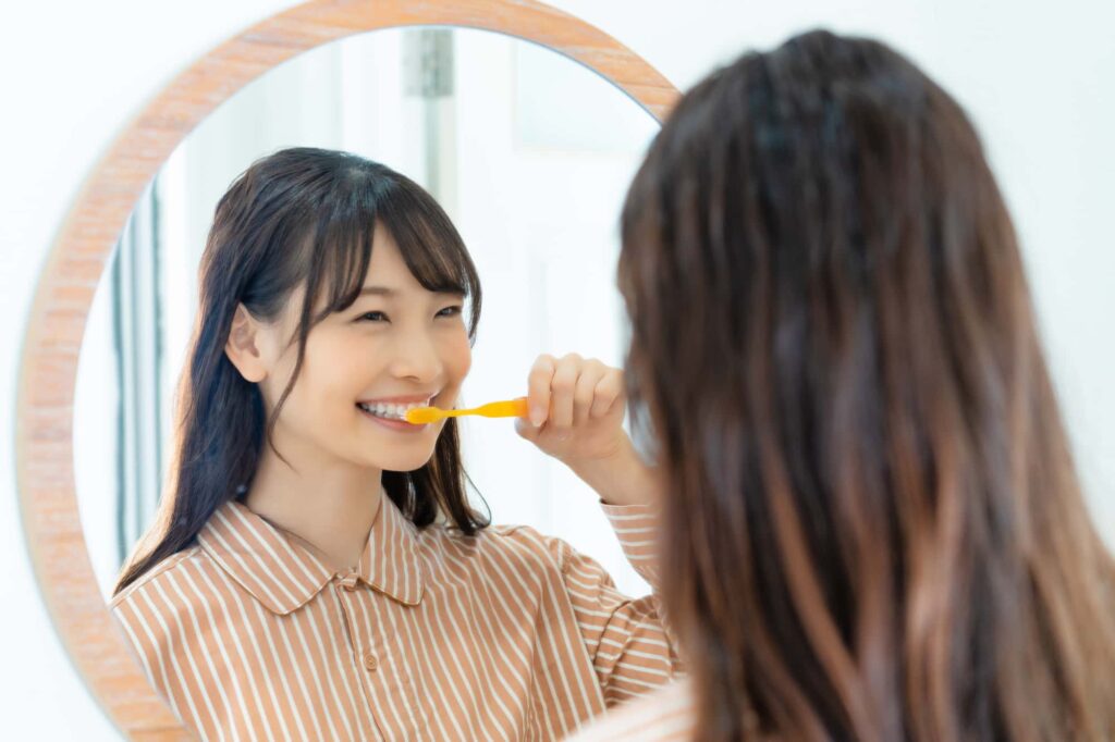 ワイヤー矯正中に鏡を見ながら歯磨きをする女性